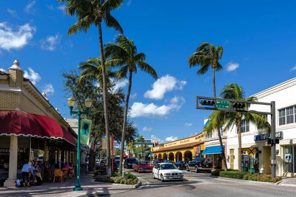 Atlantic Avenue in Delray Beach with palm trees, shops, restaurants, and cars along a sunny Florida main street.