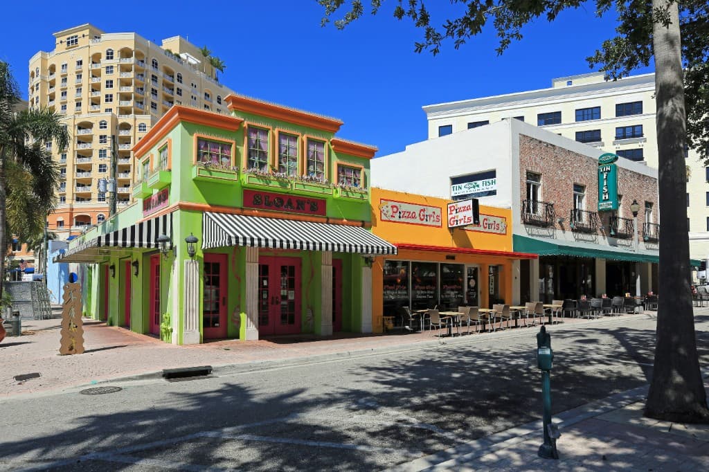 Clematis Street in West Palm Beach with colorful storefronts, restaurants, palm trees, and a sunny downtown Florida street.