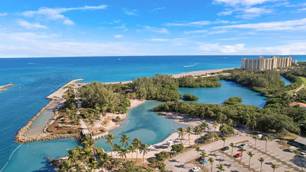 Aerial view of Jupiter Beach Park with turquoise water, palm trees, sandy shoreline, and oceanfront buildings on a sunny Florida day.