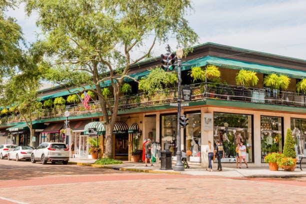 Park Avenue in Winter Park with local shops, restaurants, palm trees, and pedestrians along a sunny Florida main street.